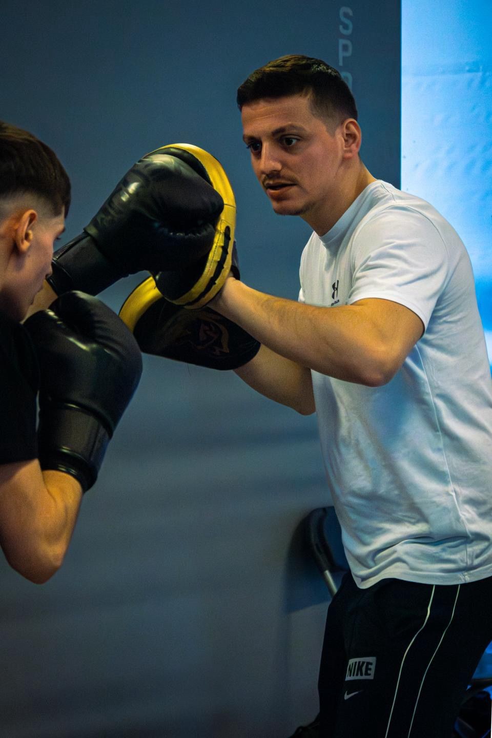 Un coach de boxe guide un élève pendant un entraînement technique, travaillant la précision et la coordination sur les paos au club Boxe La Hulpe